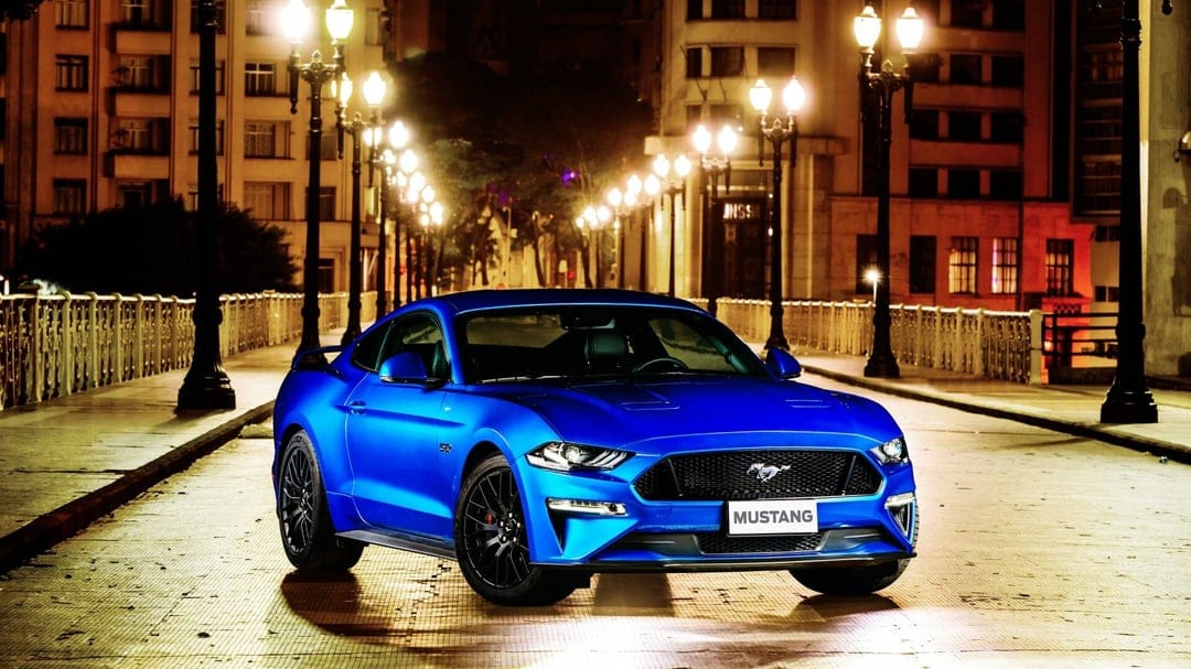 Blue Ford Mustang GT parked on a city bridge at night under glowing warm streetlights and urban buildings.