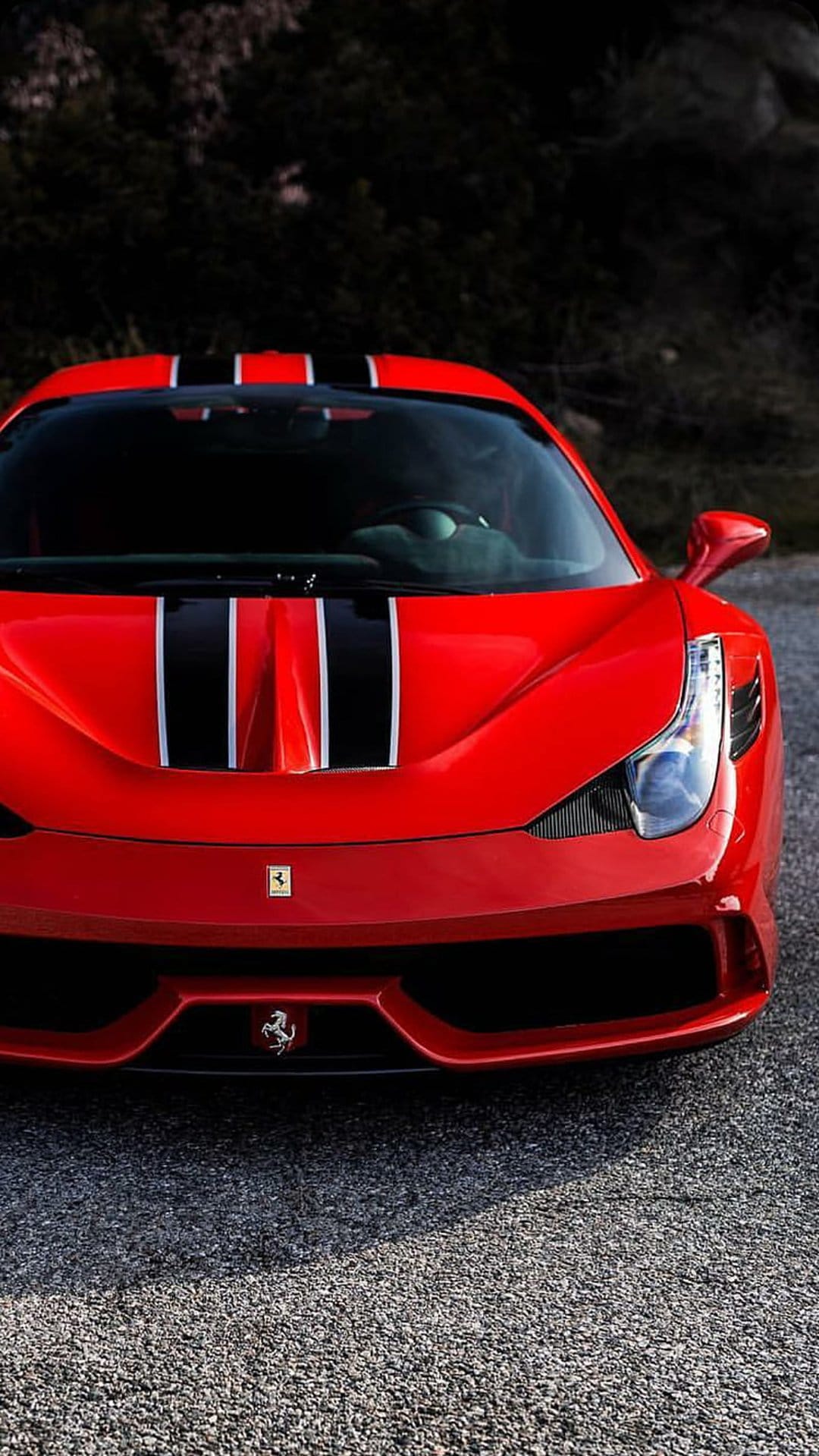Red Ferrari sports car with black and white racing stripes parked on a gravel road in a frontal portrait view.