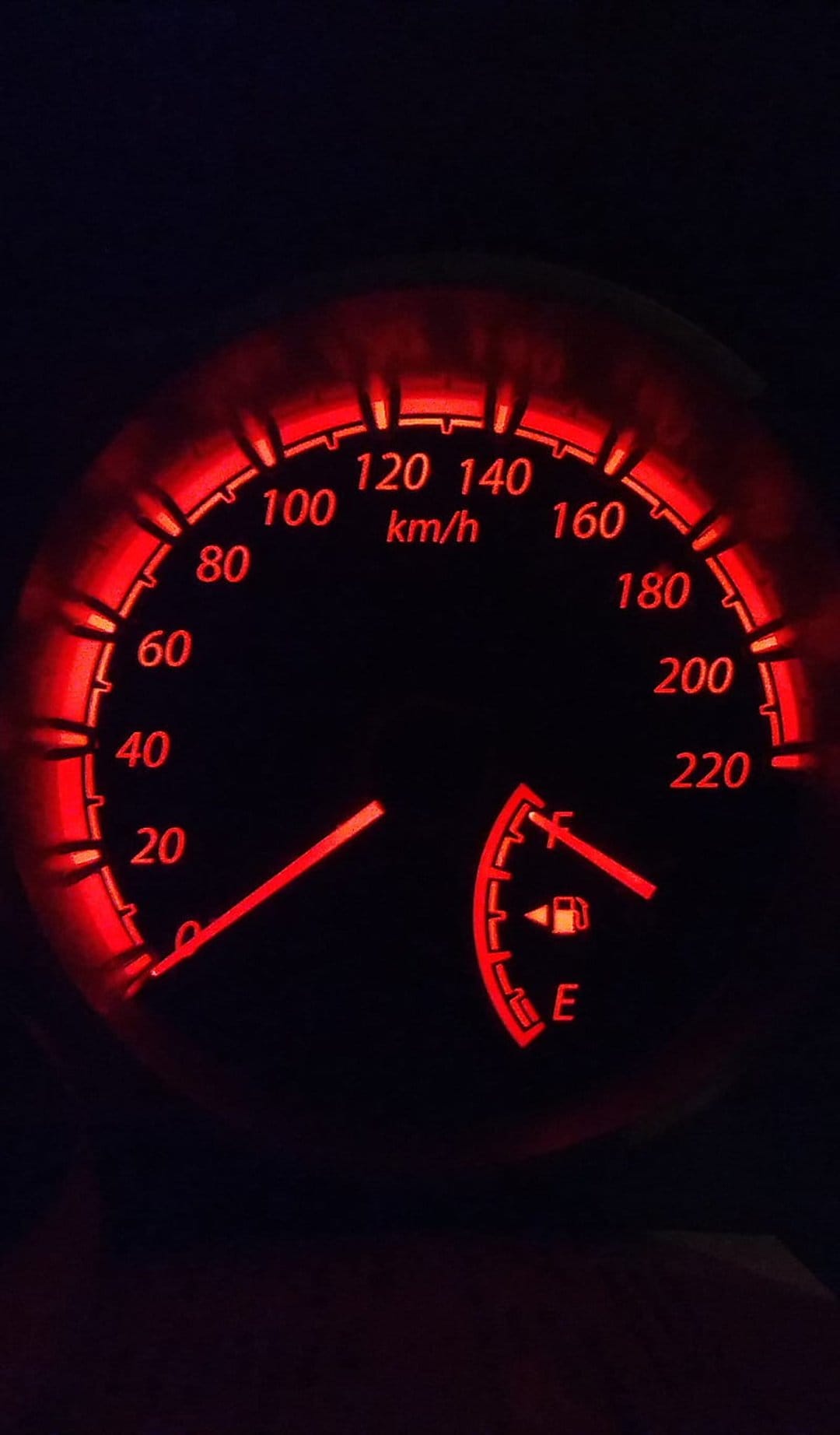 Glowing red car speedometer and fuel gauge on a dark dashboard during a night drive in a mobile-optimized view.