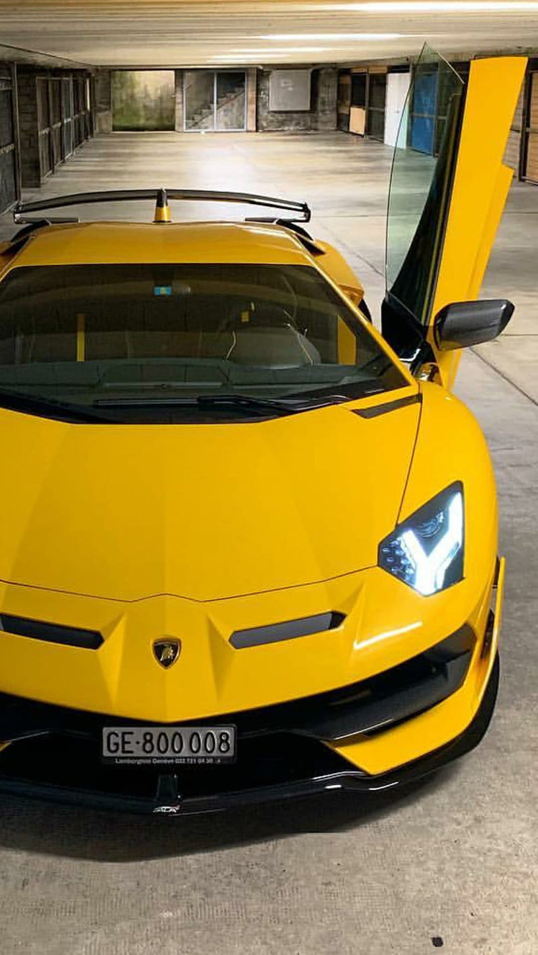 Yellow Lamborghini Aventador SVJ with open scissor doors and a large rear wing parked inside a modern garage.