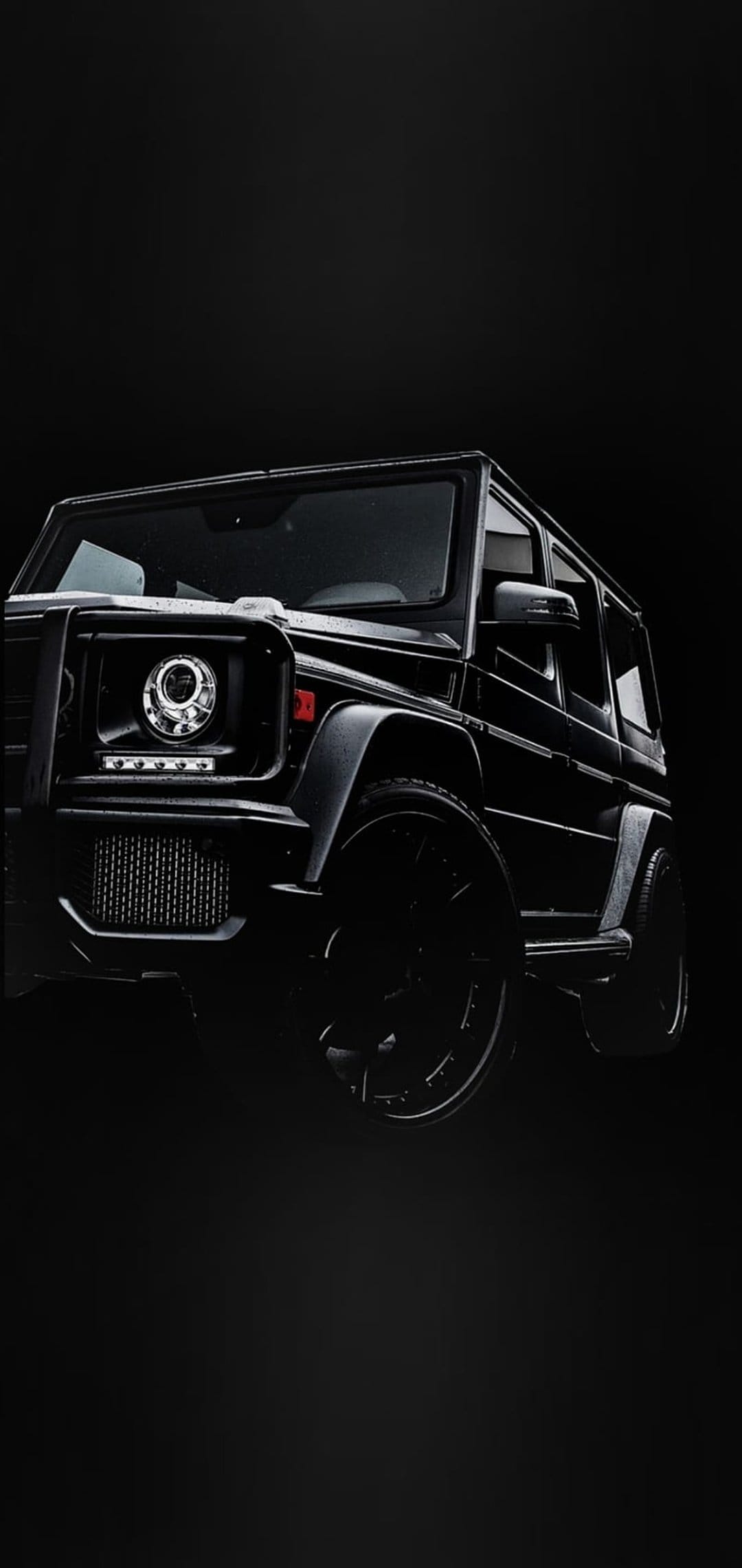 Black Mercedes G-Wagon SUV with glowing round headlights and custom wheels against a pitch-black background.
