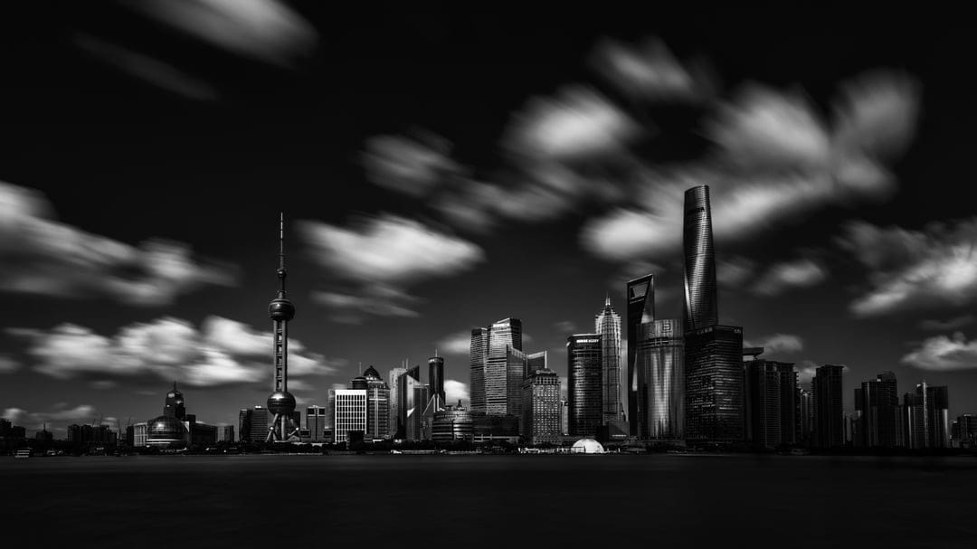 Shanghai's Pudong skyscrapers rise beneath long-exposure streaking clouds in a high-contrast monochrome scene.