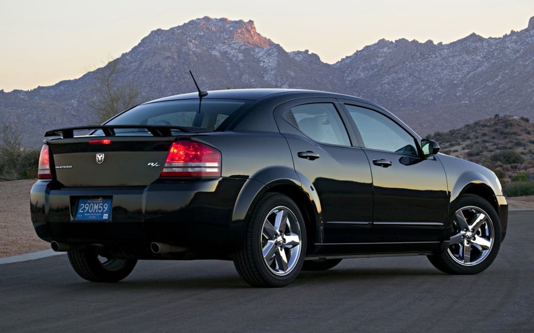 Black Dodge Avenger R/T parked on an asphalt road with rugged desert mountains under a soft twilight sky.