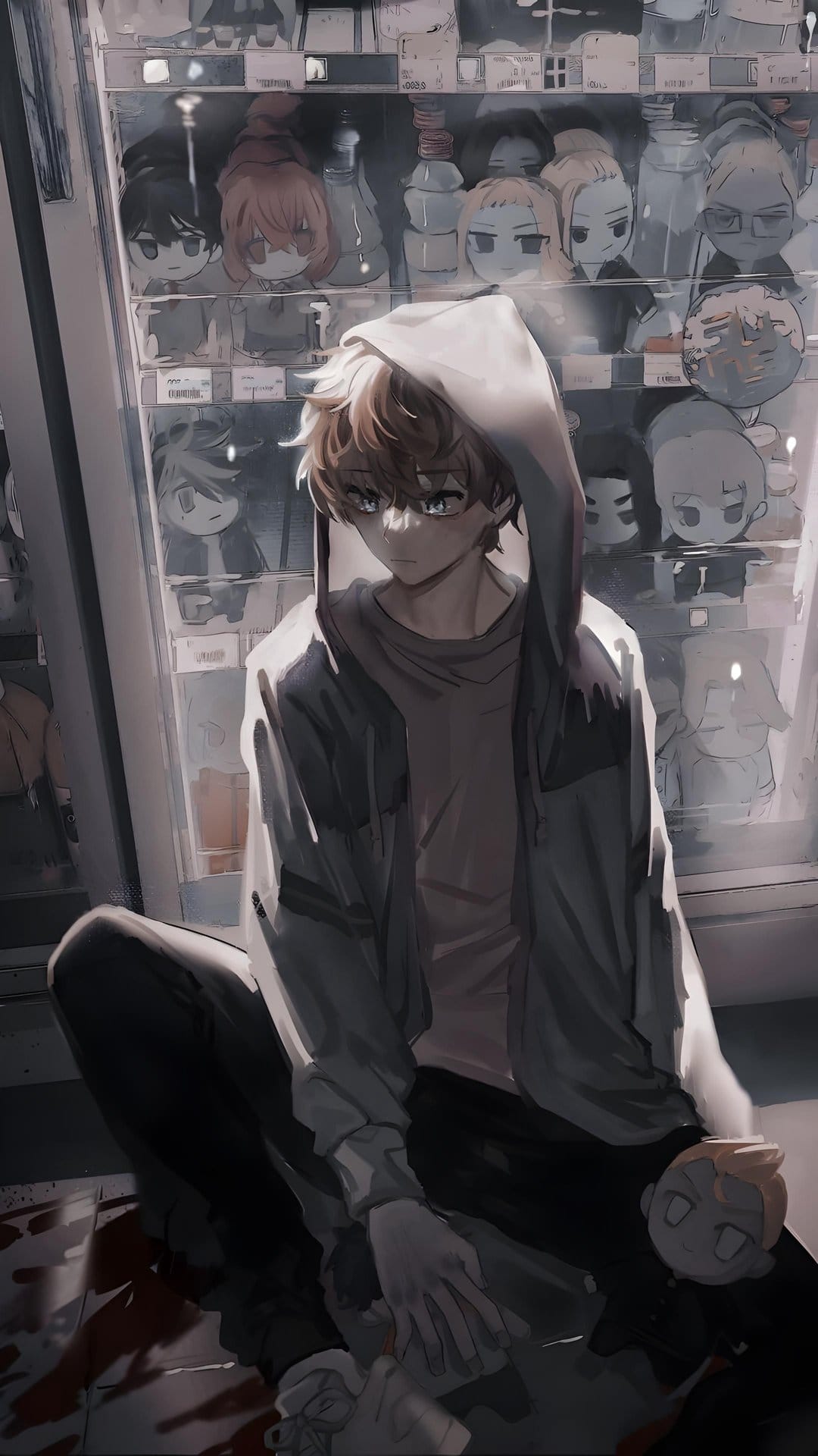 Anime boy in a grey hoodie sits before backlit gacha machines holding a small plush toy in a dim room.