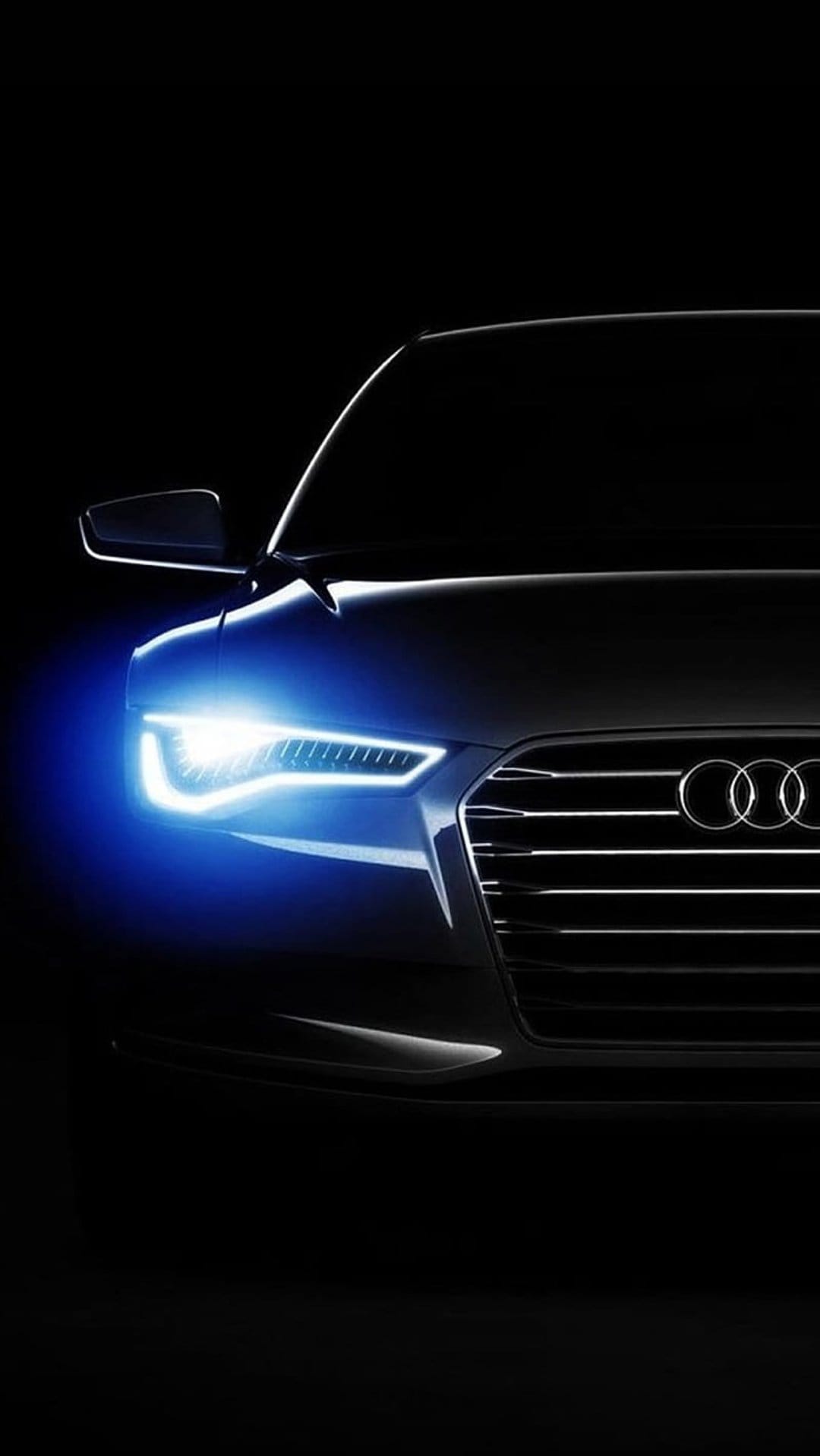 Audi LED headlight with a vibrant blue glow and chrome rings visible against a solid black background at night.