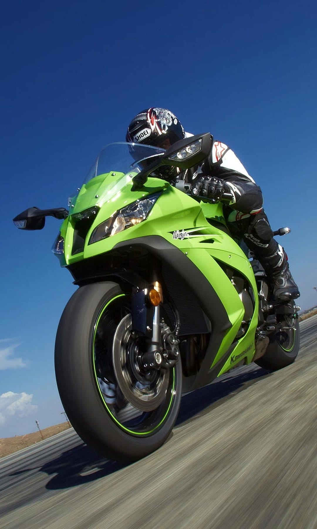 Kawasaki Ninja motorcycle with rider in green gear leaning into an asphalt curve under a clear blue sky.