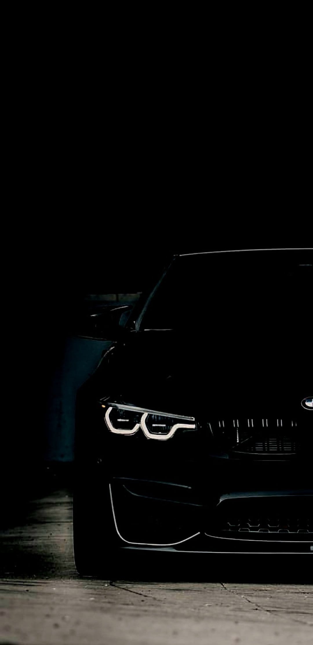 BMW M4 LED headlights and grille glow in a dark concrete garage with dramatic low-angle shadows and reflections.