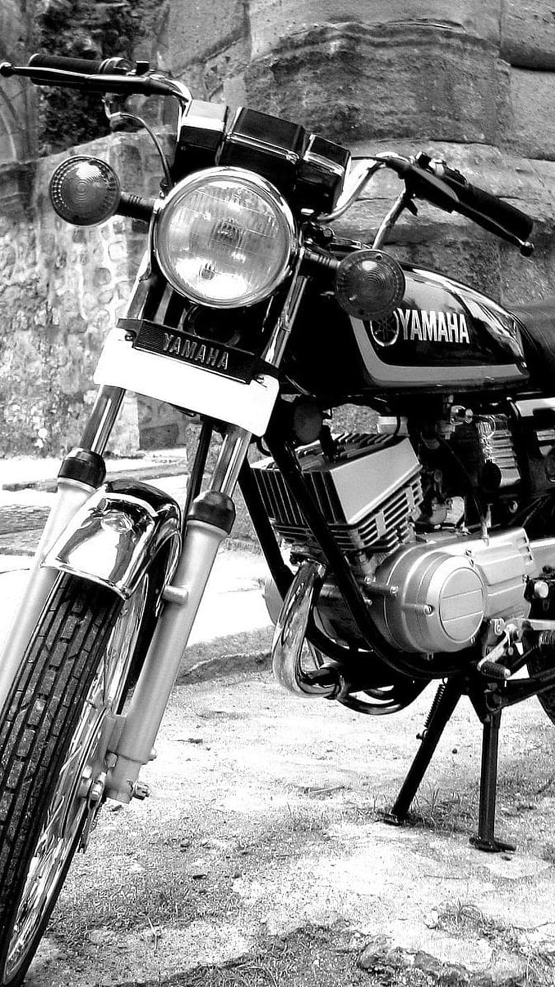 Yamaha vintage motorcycle headlight and engine detail set against a textured stone wall in black and white.