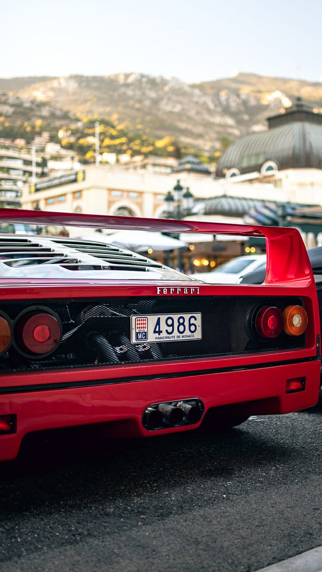 Ferrari F40 rear view with a red spoiler, quad exhaust pipes, and a Monaco license plate on a European street.