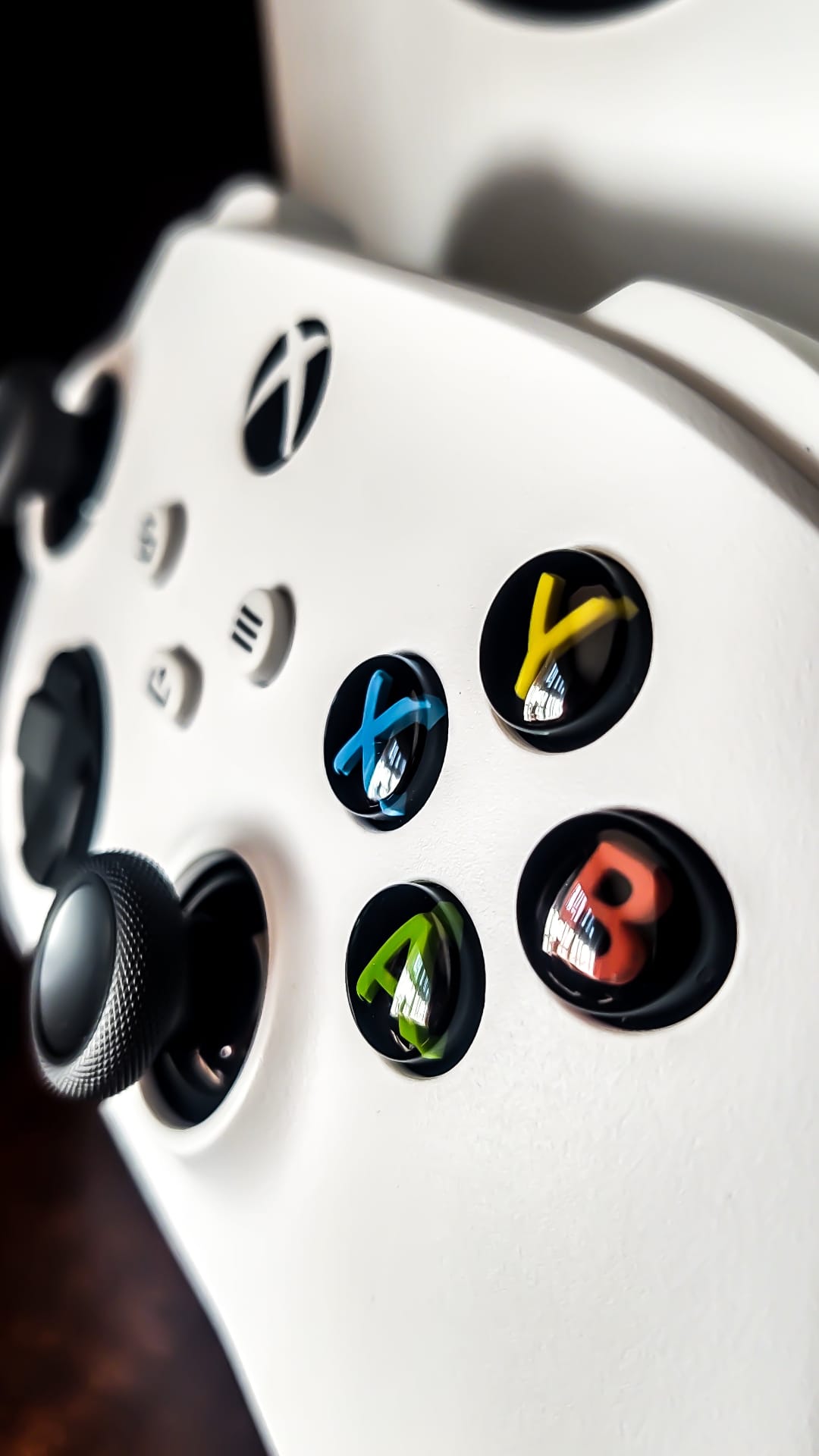 White Xbox controller face buttons and a textured joystick captured in a sharp macro shot with soft lighting.