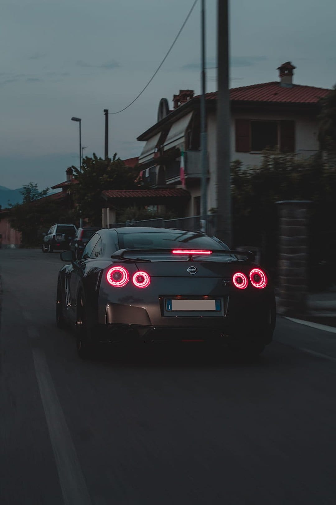 Nissan GT-R rear exterior featuring glowing red circular taillights against a blurred twilight suburban road.