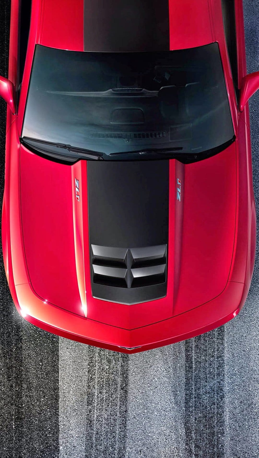Red Chevrolet Camaro ZL1 with a black racing stripe viewed from above on textured asphalt with tire tracks.