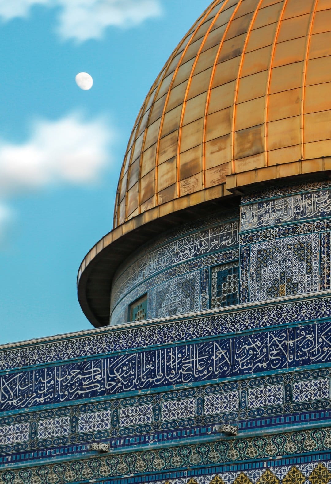 Golden Dome of the Rock with blue calligraphy under a pale moon and soft clouds in a bright blue sky.