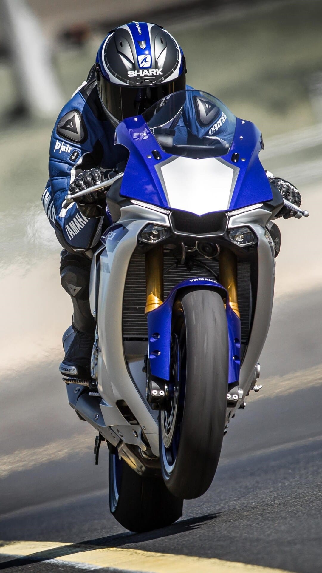 Yamaha R1 motorcyclist performing a wheelie on an asphalt road with the front tire lifted high in the air.