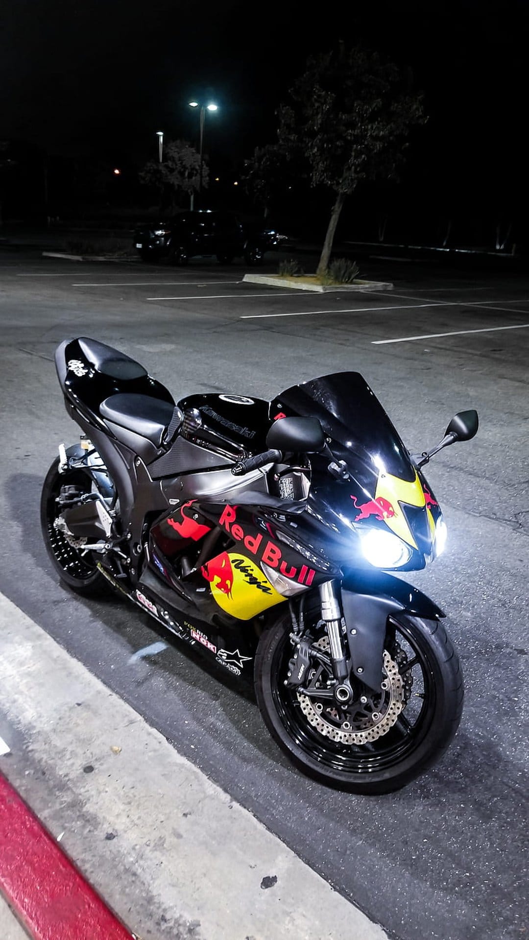 Black Kawasaki Ninja motorcycle with Red Bull decals at night featuring glowing headlights and yellow accents.