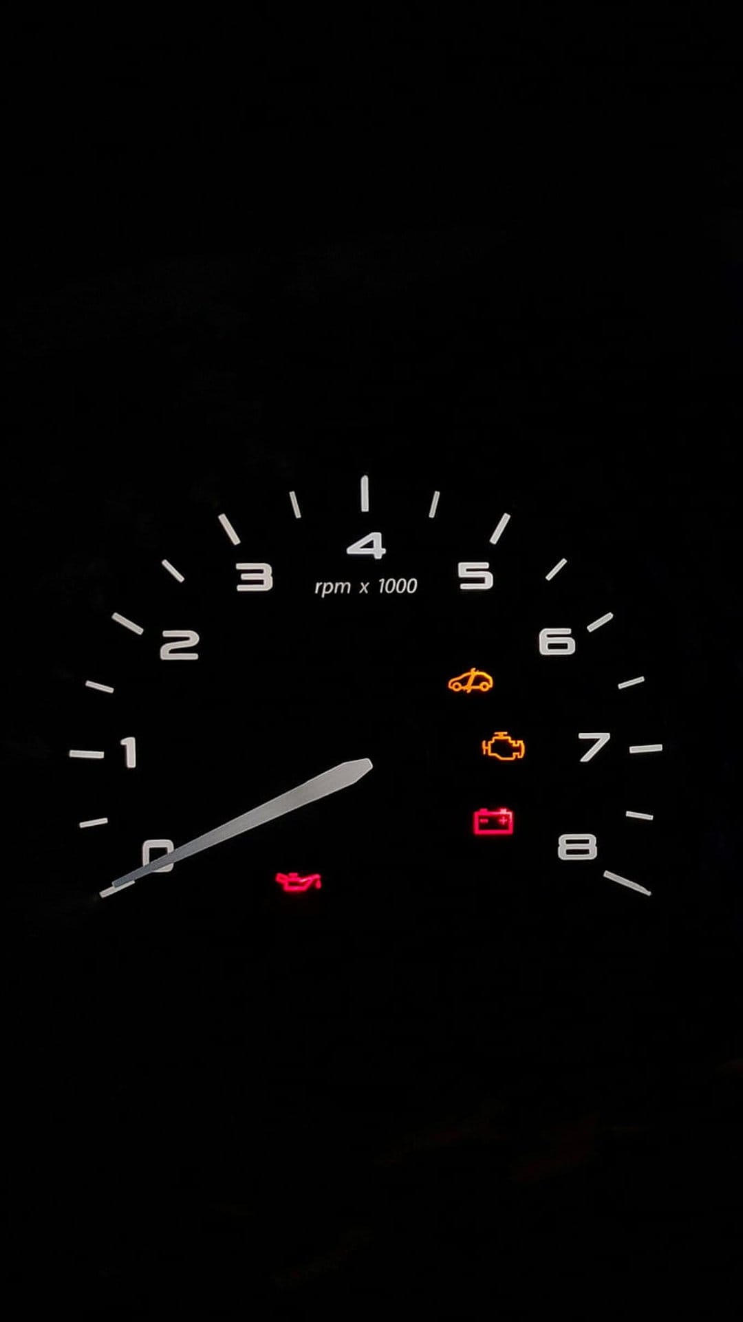 Car tachometer and glowing dashboard warning lights illuminated in amber and red during a nighttime drive.