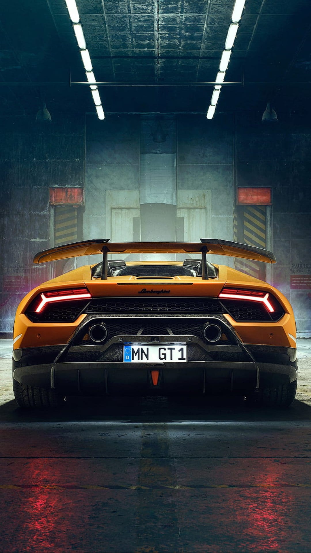 Orange Lamborghini Huracan GT1 rear view in a dark industrial garage with red reflections on a wet floor.