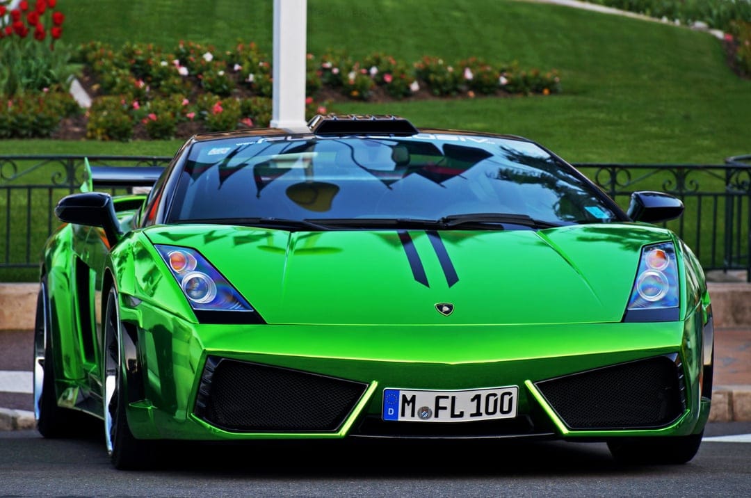 Shiny chrome green Lamborghini Gallardo with a widebody kit and roof scoop parked in a lush garden landscape.
