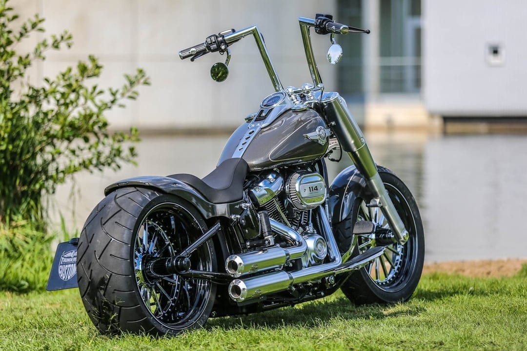 Custom Harley-Davidson motorcycle with wide rear tire and chrome engine parked on grass near water.