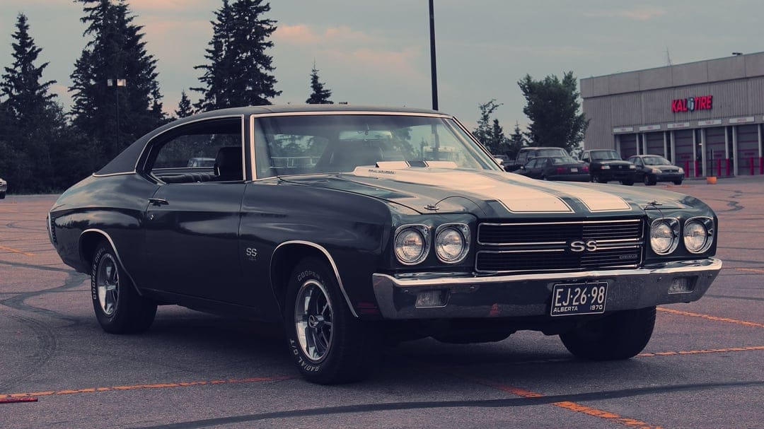 Dark green 1970 Chevrolet Chevelle SS with white racing stripes parked in a lot during a moody cloudy sunset.