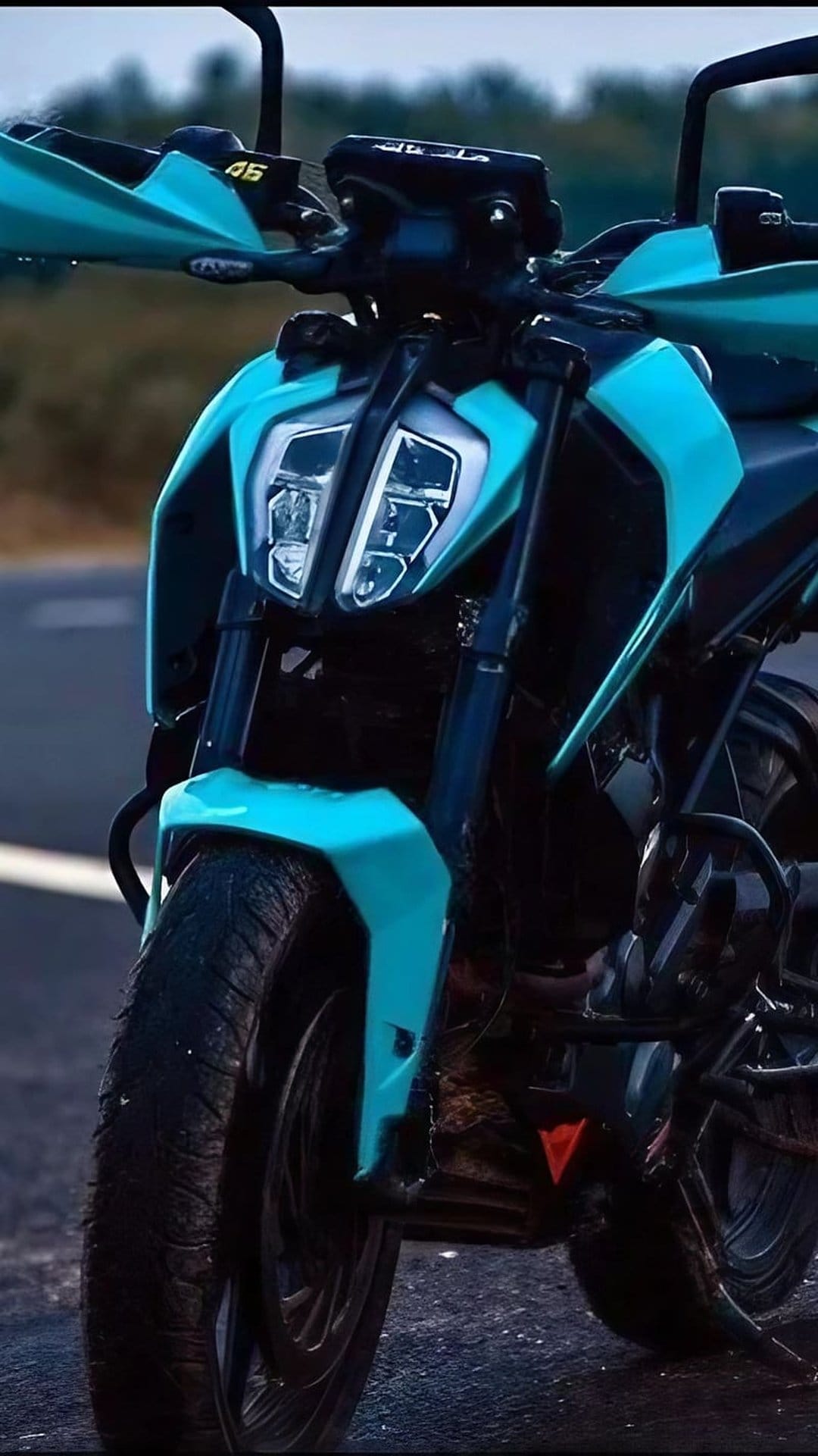 Turquoise KTM motorcycle front fairing with sharp LED headlights and textured tires on an asphalt road surface.