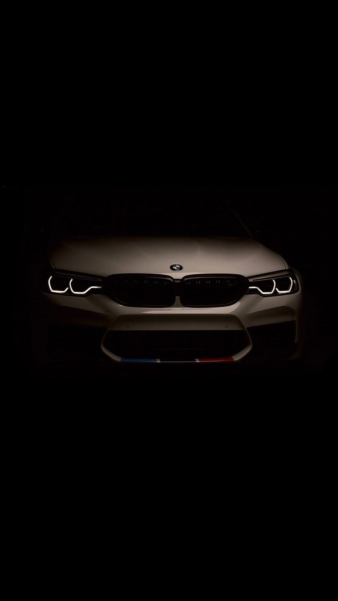 BMW M5 front end with glowing circular headlights and a white kidney grille against a pitch black background.