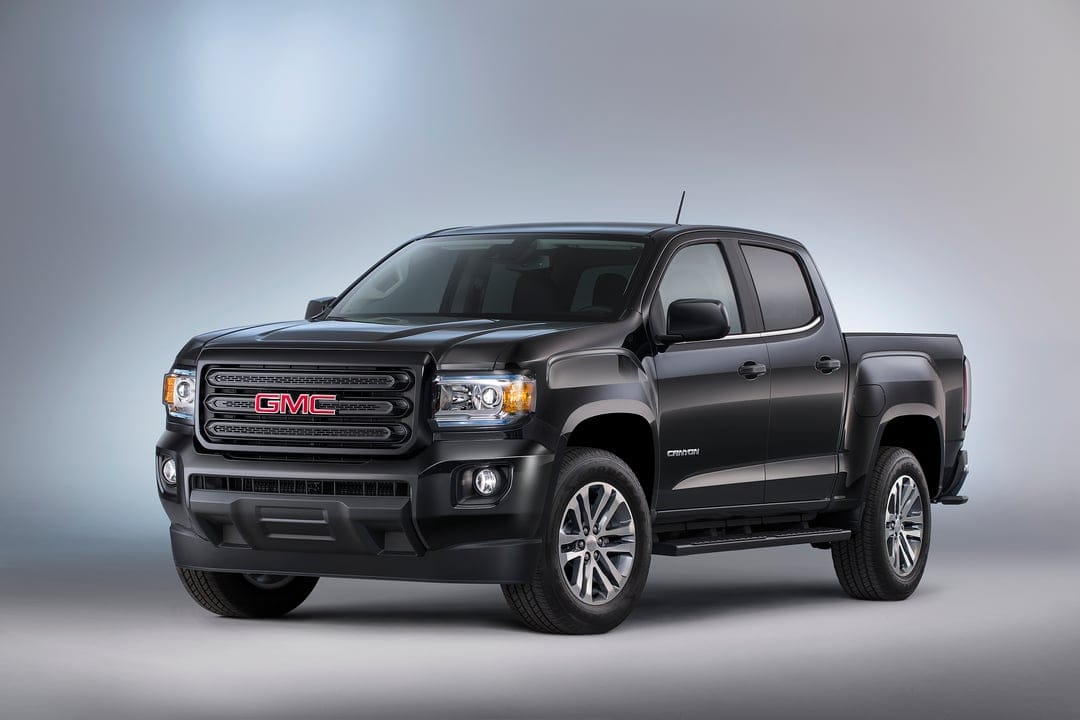 Black GMC Canyon pickup truck with silver wheels on a soft grey studio background with cool lighting.