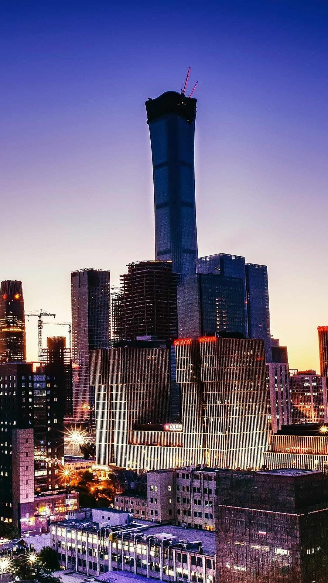 Beijing skyscrapers including the CCTV building glow with office lights under a blue and orange twilight sky.
