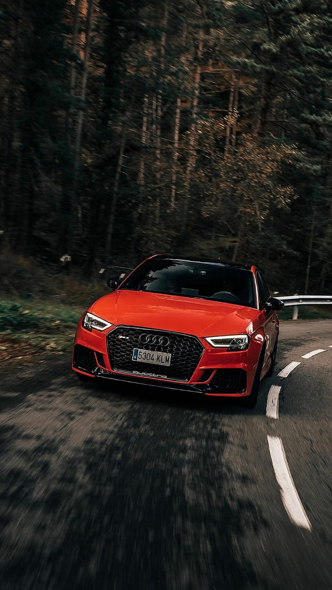 Red Audi RS3 sports car speeds through a dense green forest on a winding asphalt road with realistic motion blur.