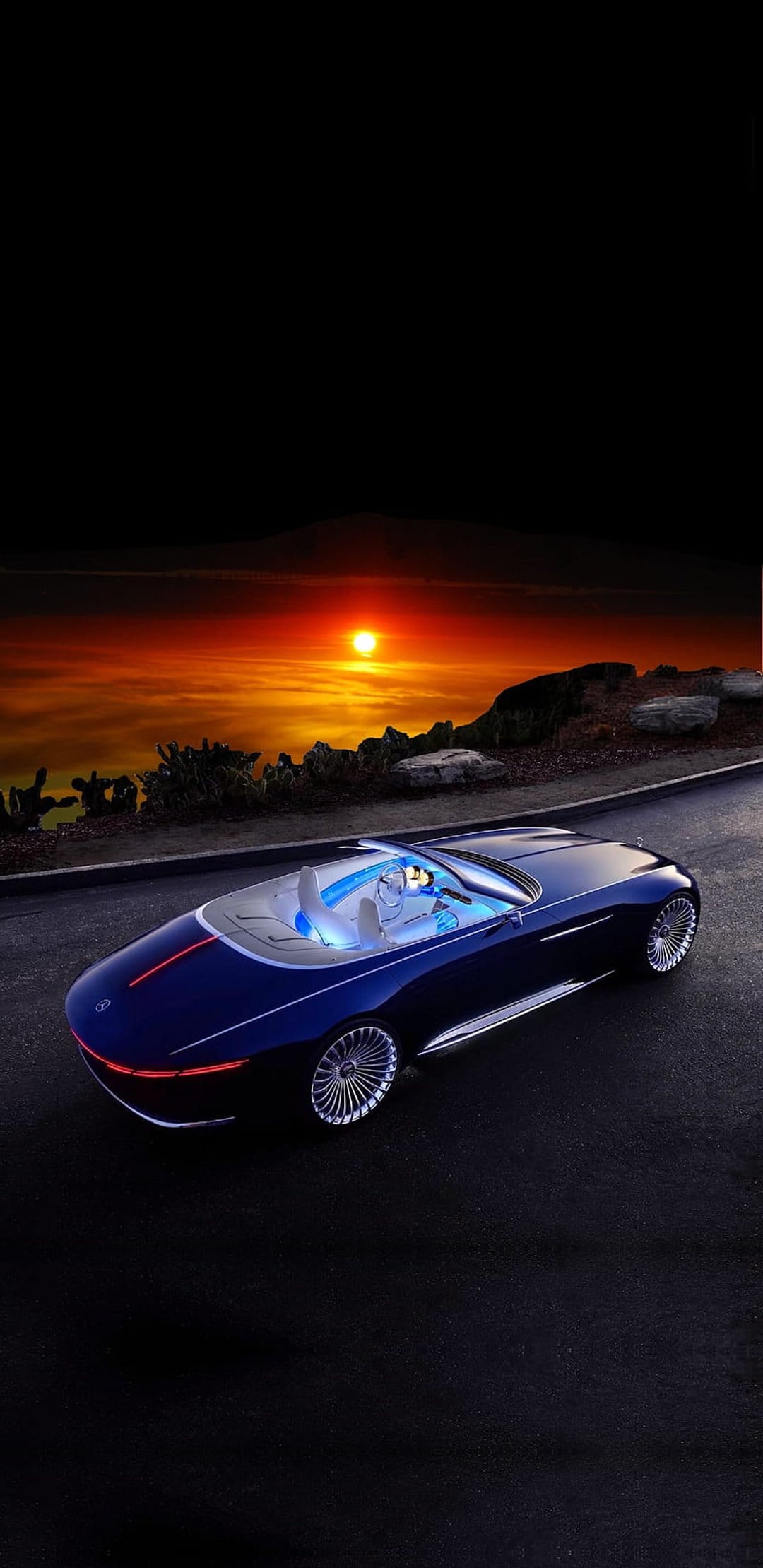Dark blue luxury convertible car parked on a desert highway under a vivid orange and red sunset sky at dusk.
