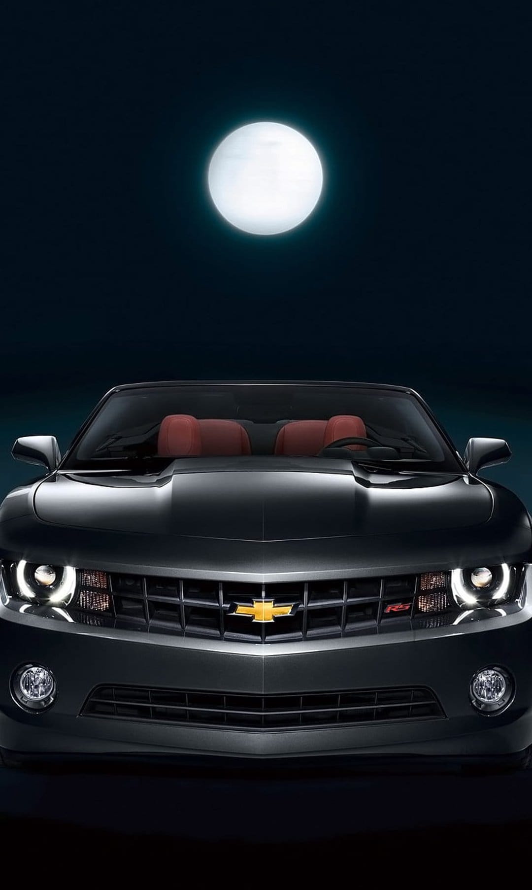 Black Chevrolet Camaro convertible with red seats parked at night under a full moon with glowing headlights.