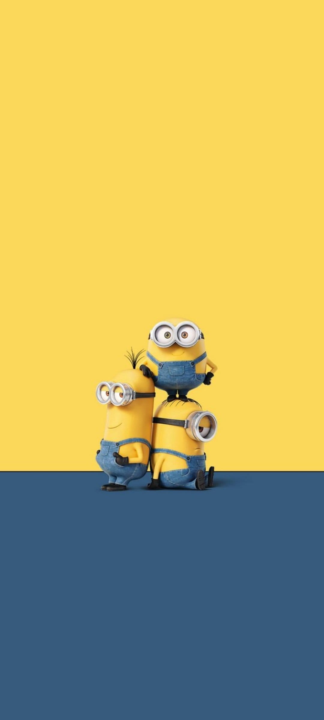 Three Minions stack vertically wearing goggles and overalls against a split yellow and navy blue backdrop.