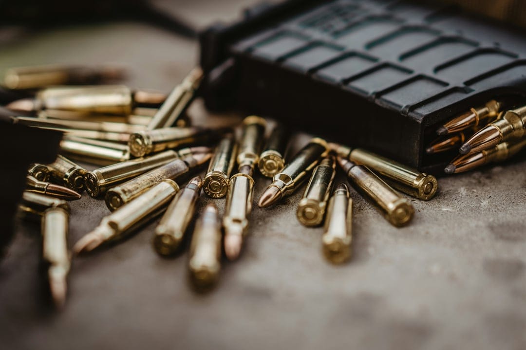 Brass rifle cartridges and a black polymer magazine rest on a textured stone surface with a shallow depth of field.