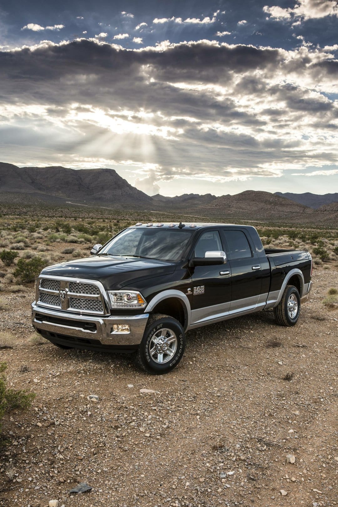 Black Ram 2500 Heavy Duty truck in a desert landscape under a cloudy sky with crepuscular sun rays.