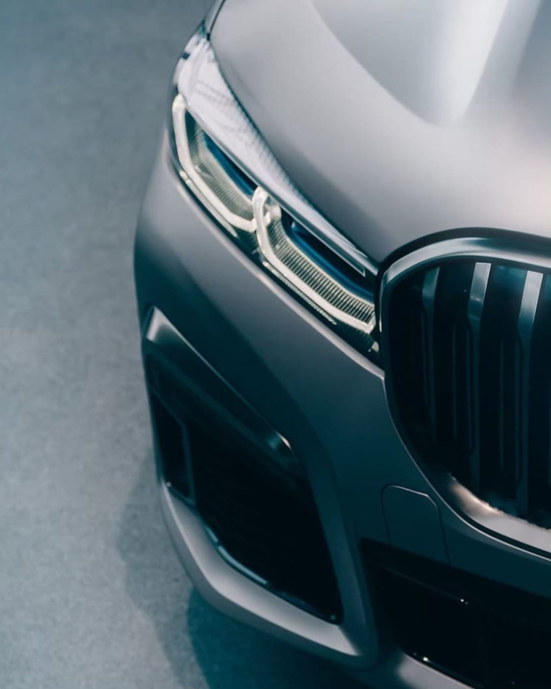 BMW LED headlight and vertical kidney grille on a sleek silver car body with sharp reflections and metallic textures.