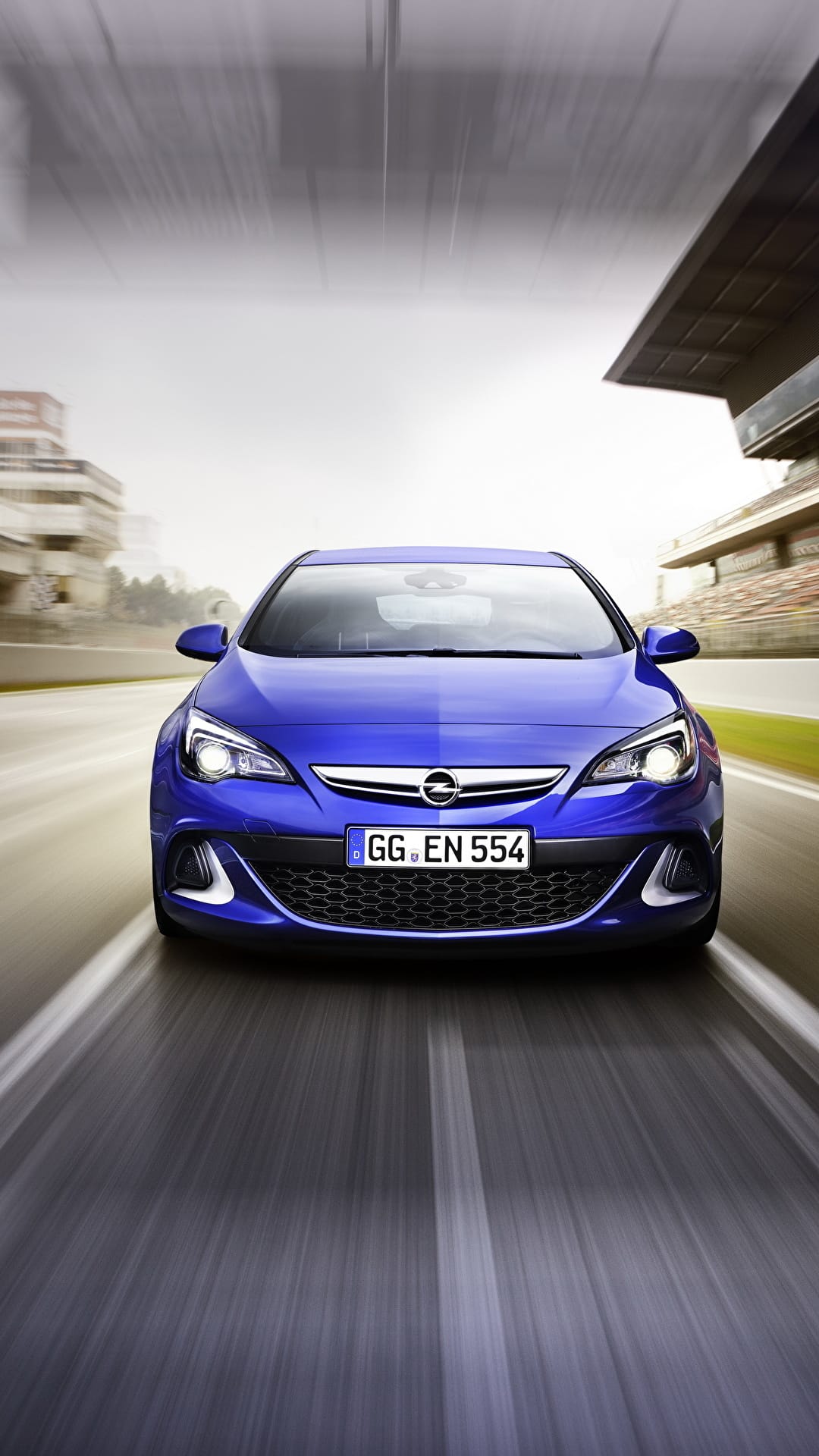 Front view of a blue sports car speeding on a racetrack with intense motion blur and grandstands in the background.