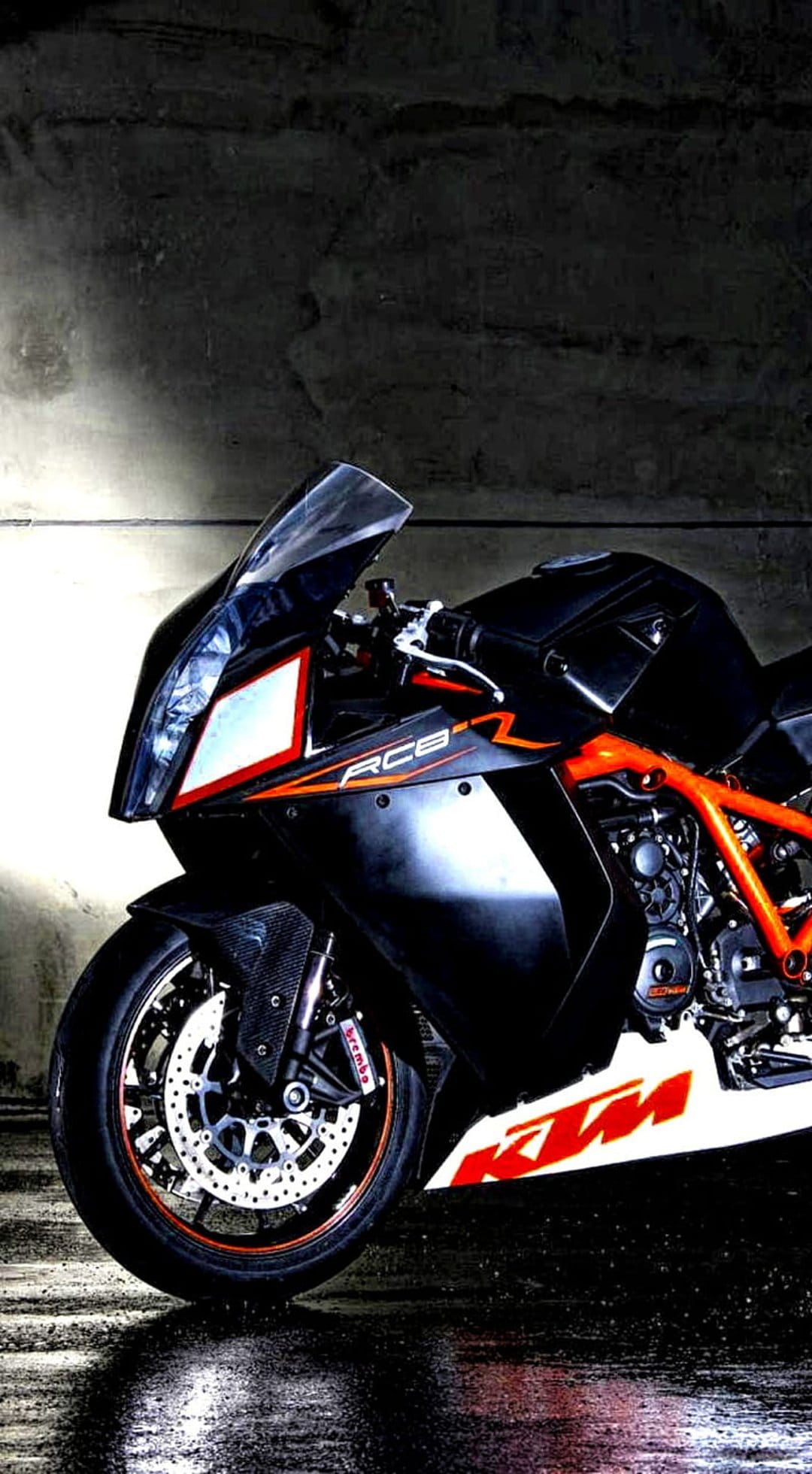 KTM RC8 superbike with an orange trellis frame and black bodywork parked on wet asphalt under dramatic lighting.