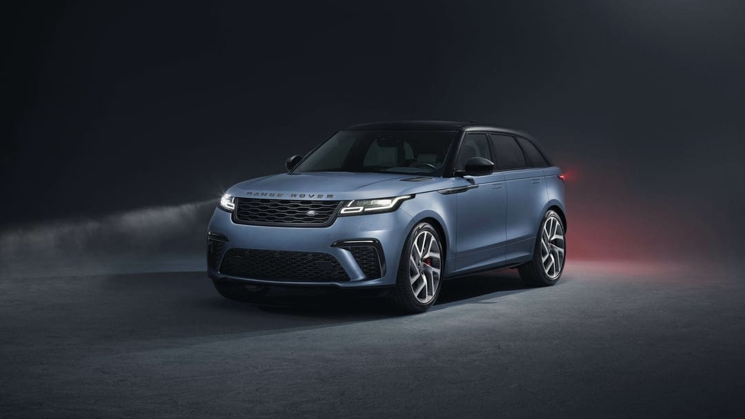 Light blue Range Rover Velar with glowing headlights and silver wheels in a dark, atmospheric studio.