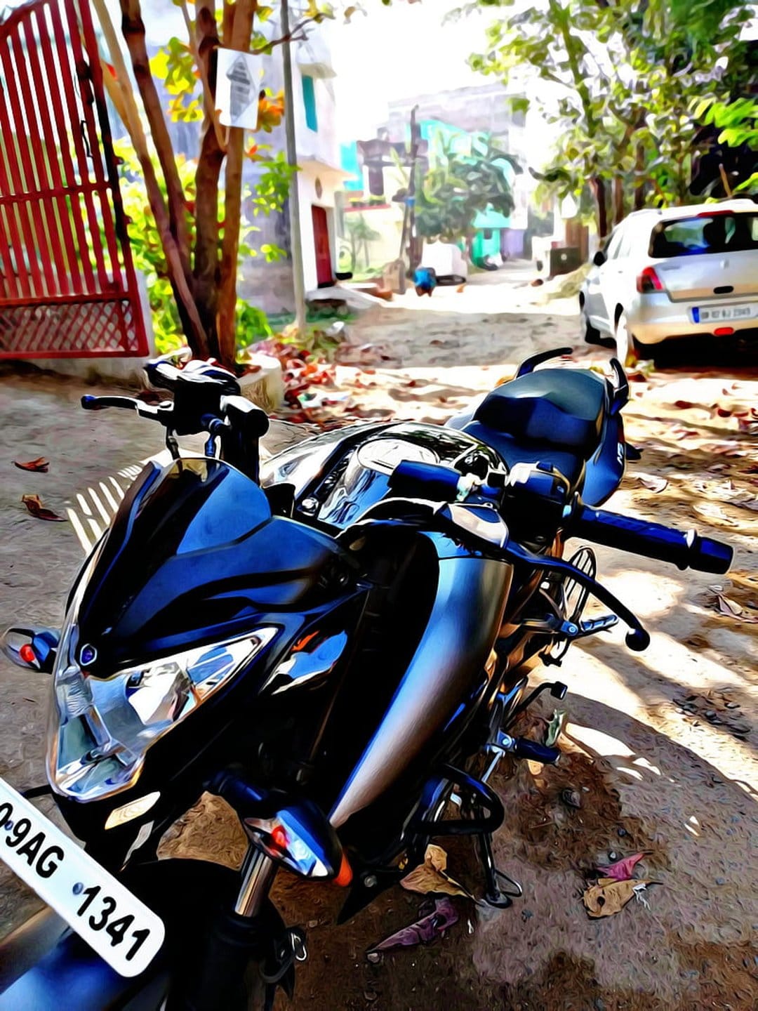 Black motorcycle with a glossy finish parked on a sunlit city street near a silver car and urban greenery.