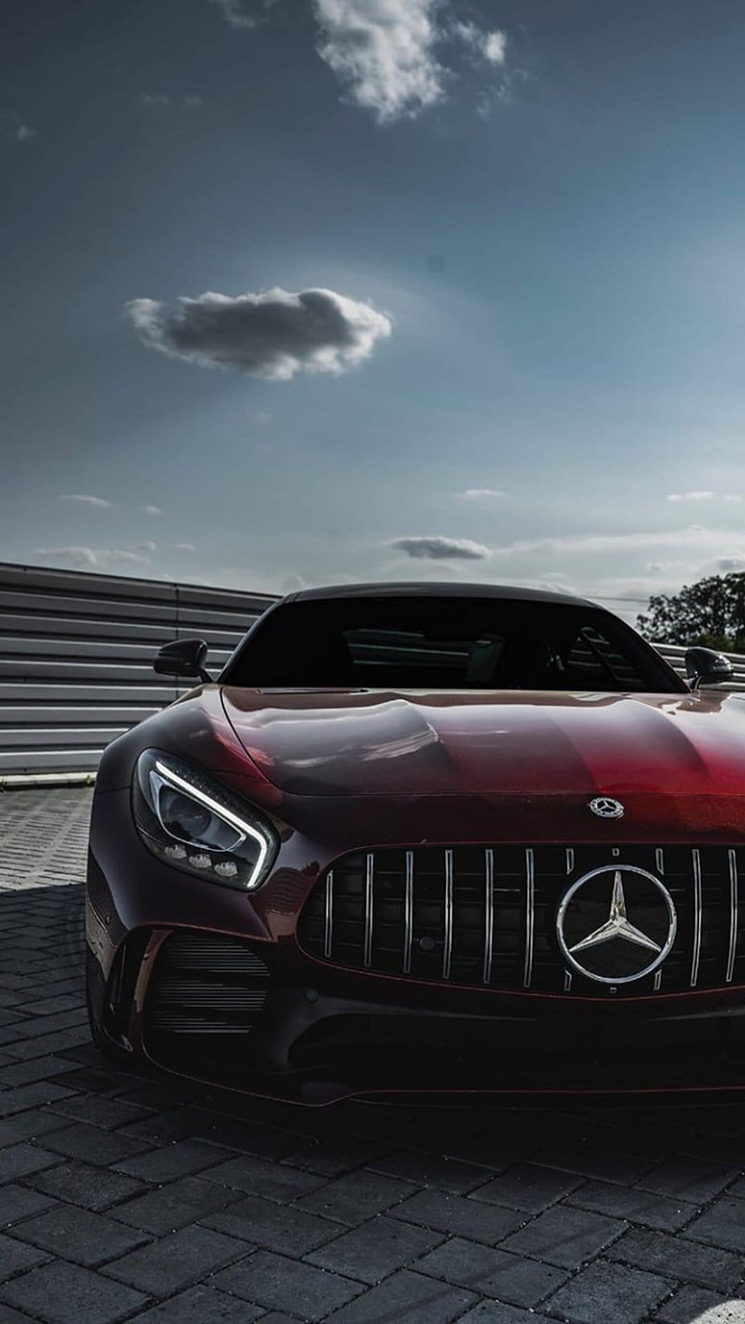 Red Mercedes-AMG GT front grille with chrome slats and LED headlights on a textured brick surface under a grey sky.