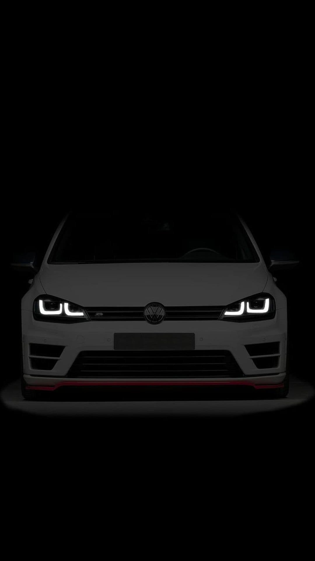 White Volkswagen Golf R front grille with glowing LED headlights and red accents against a black background.