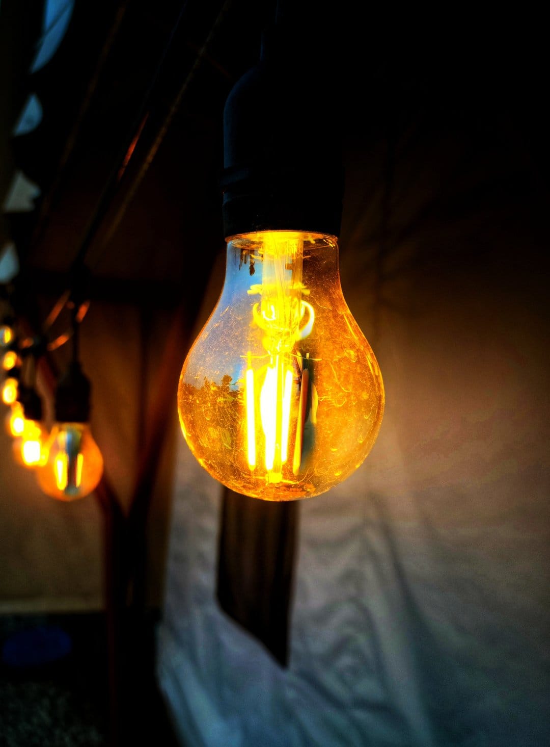 Vintage Edison bulb with a visible glowing filament hangs in focus against a backdrop of blurry golden bokeh.