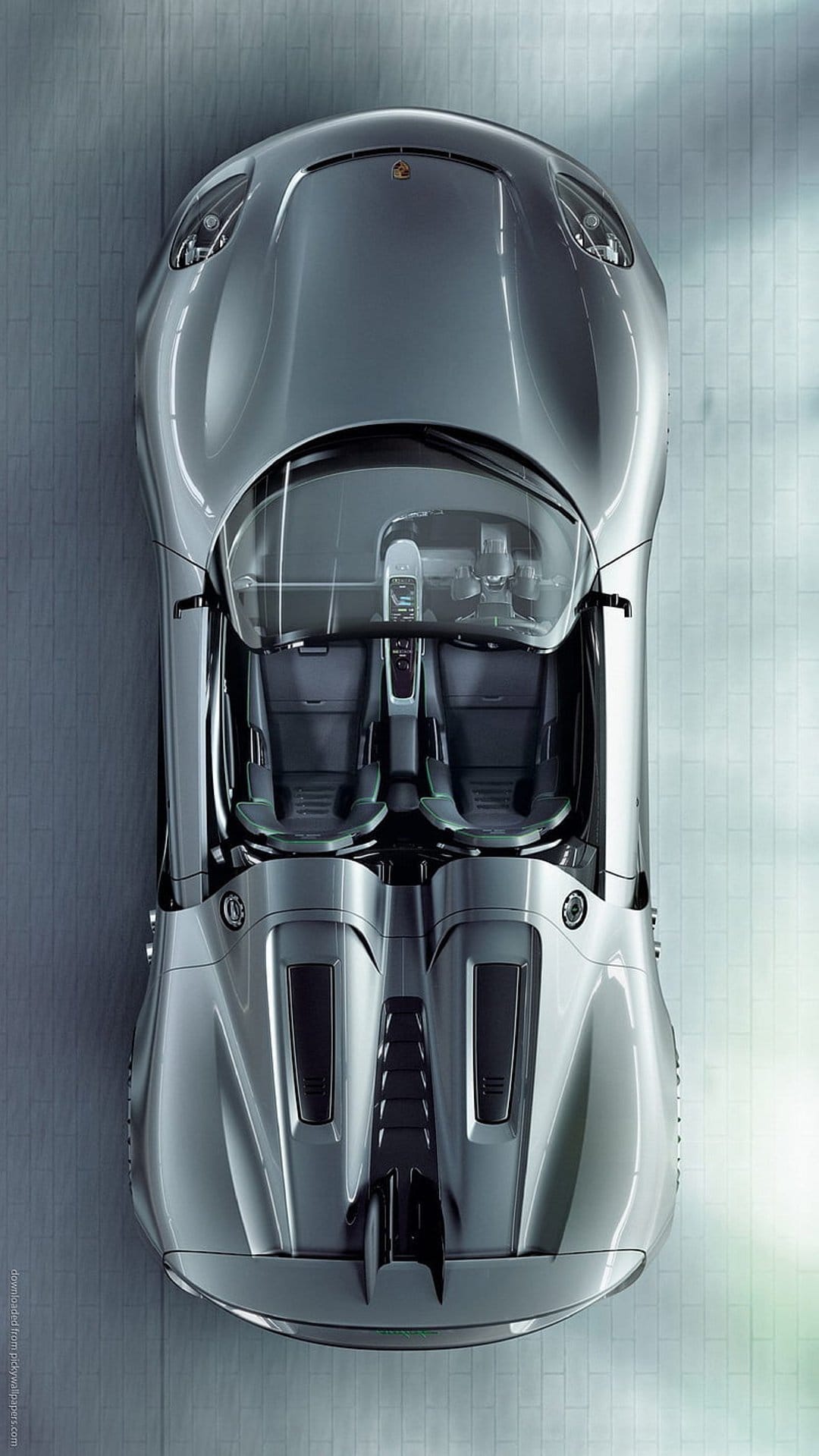 Silver Porsche sports car seen from above, showing a glass roof, bucket seats, and metallic engine cover.