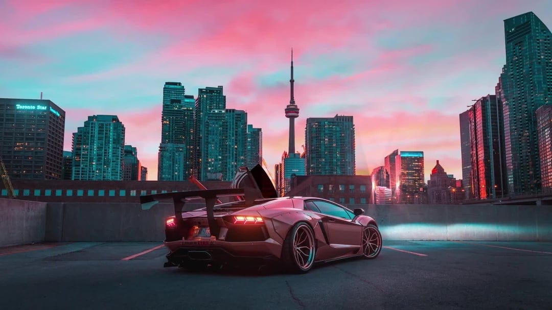 Modified Lamborghini Aventador parked on a rooftop with the Toronto CN Tower and pink sunset in the background.
