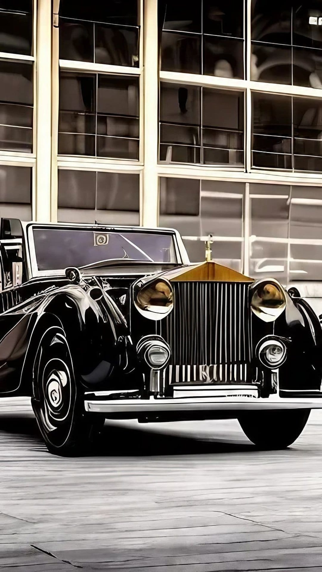 Black vintage Rolls-Royce convertible with a golden hood ornament parked on a polished wooden floor indoors.