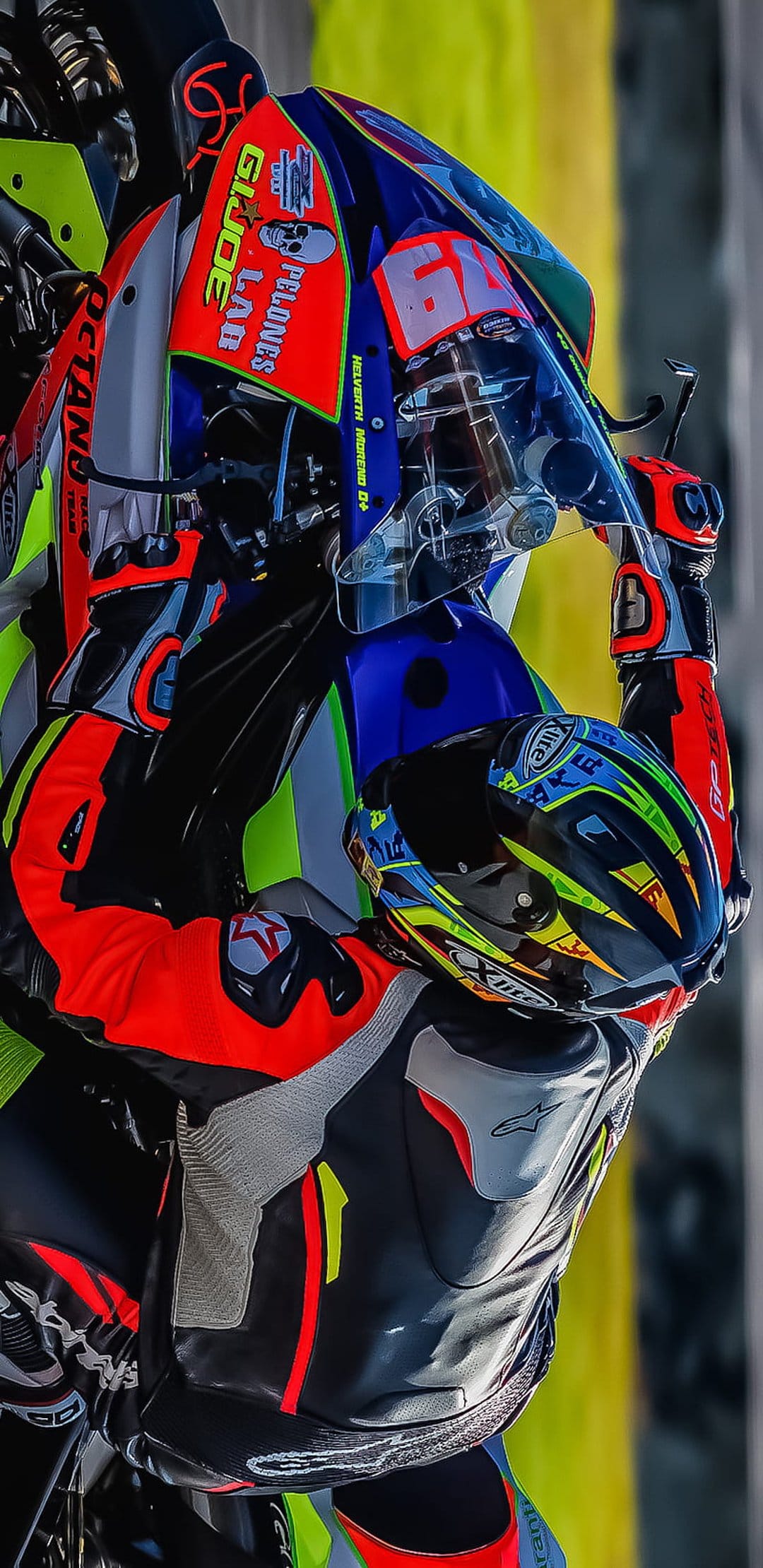 Motorcyclist in a vibrant racing suit with neon orange accents and a detailed helmet featuring sponsor logos.