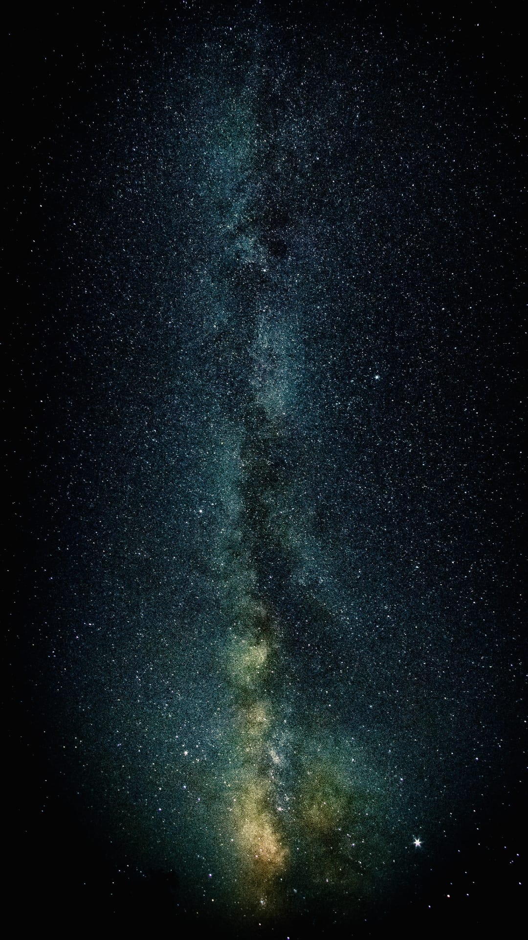 Milky Way galaxy's luminous band of stars and colorful nebulae stretching across a dark vertical night sky view.