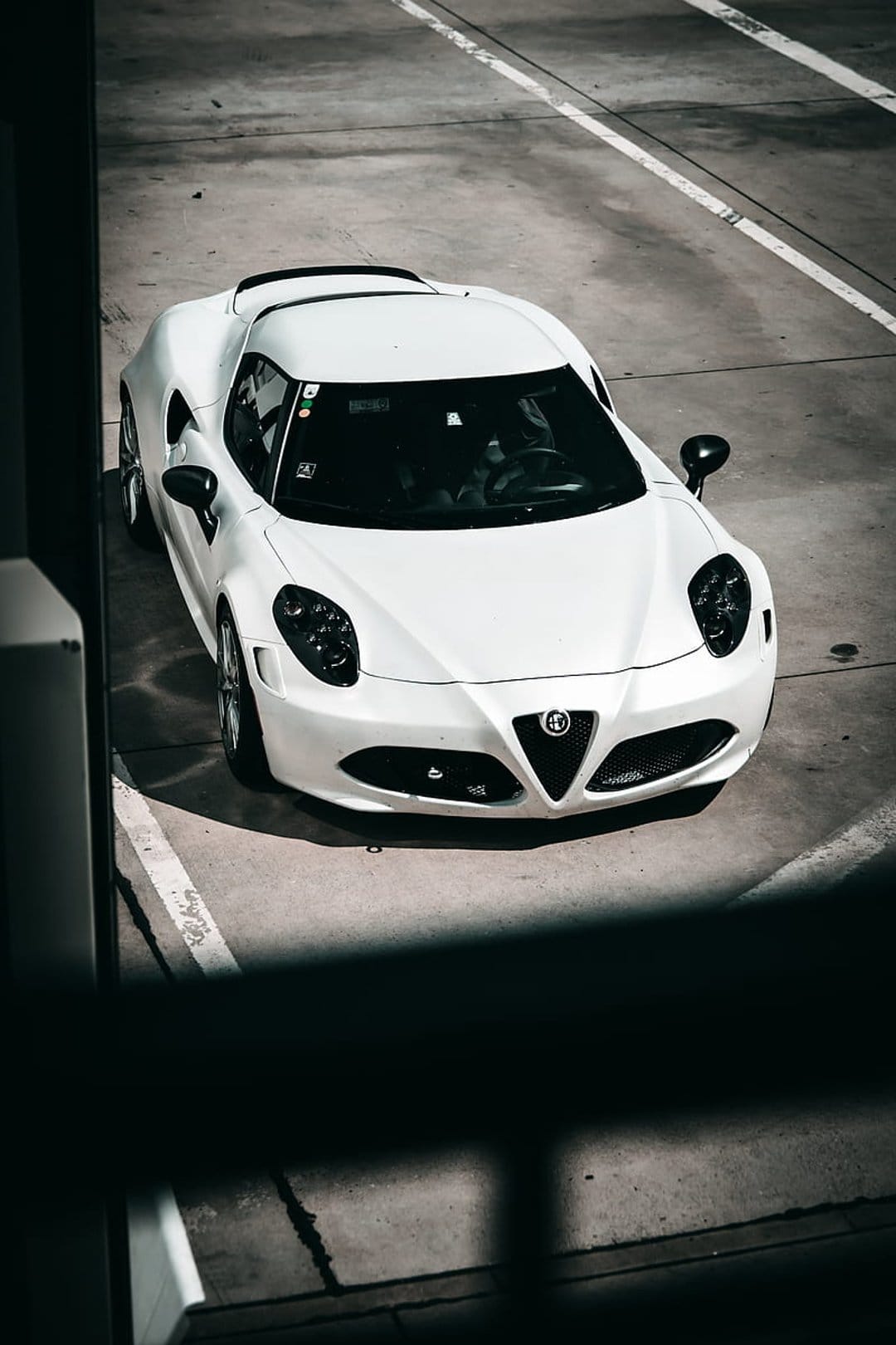 White Alfa Romeo 4C sports car parked on grey concrete with white lines seen from a direct overhead perspective.