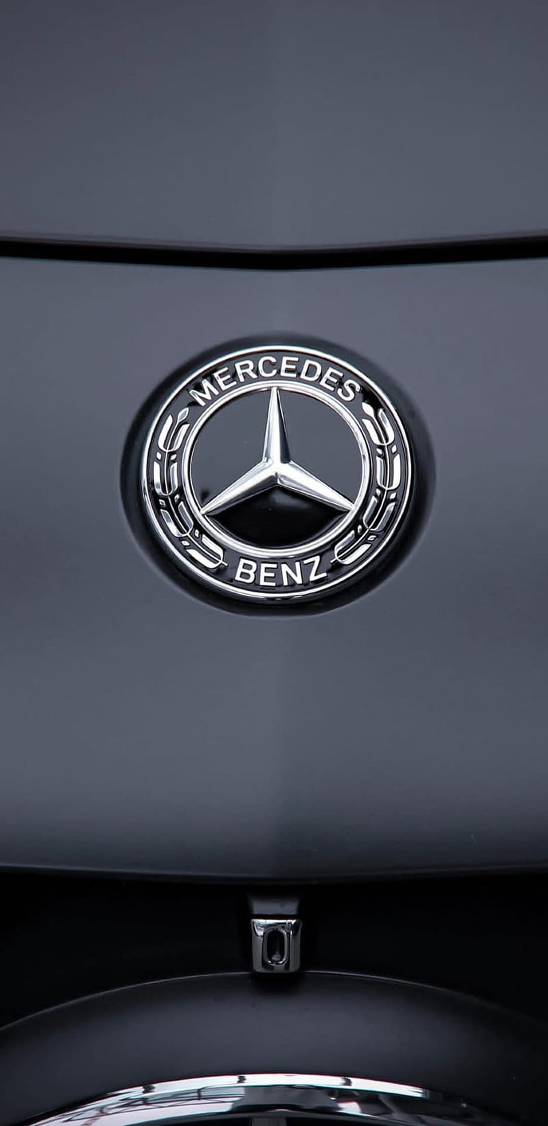 Silver Mercedes-Benz three-pointed star emblem mounted on a reflective black car hood with sharp chrome details.