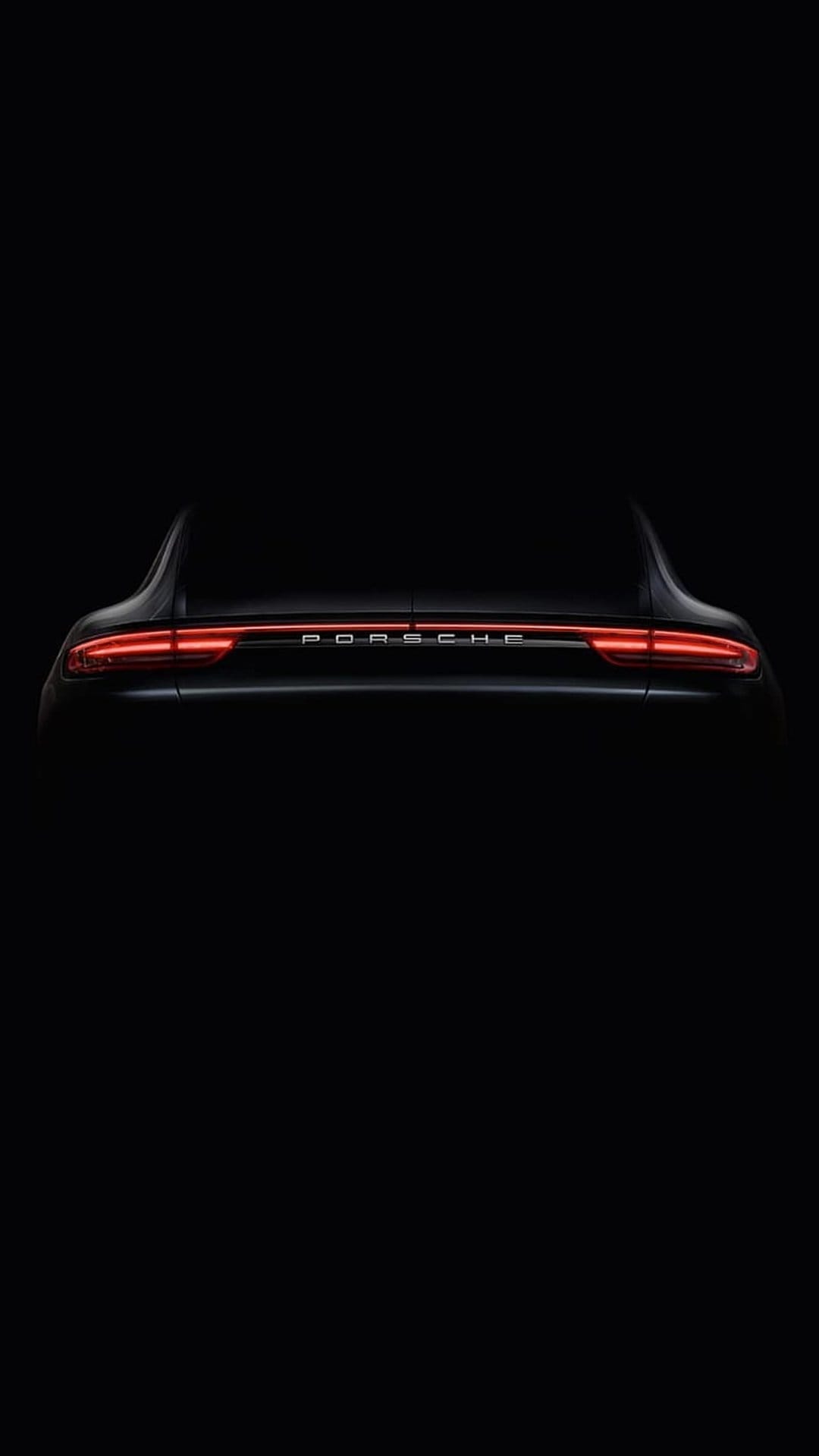 Red LED taillight strip on a black Porsche sports car glowing intensely within a dark, shadowed environment.